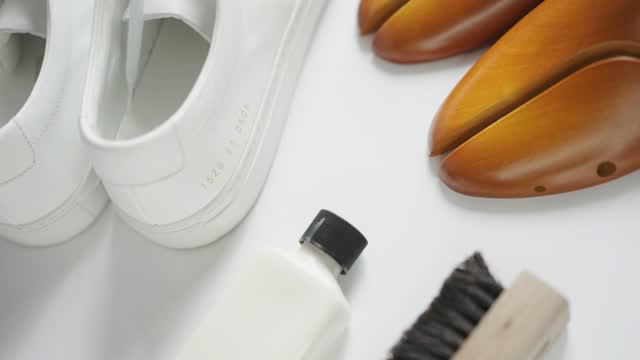 Weiße Schuhe neben einer Bürste und einer Flasche Reiniger