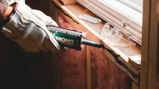 Person zieht eine Silikonfuge an einem Fensterrahmen