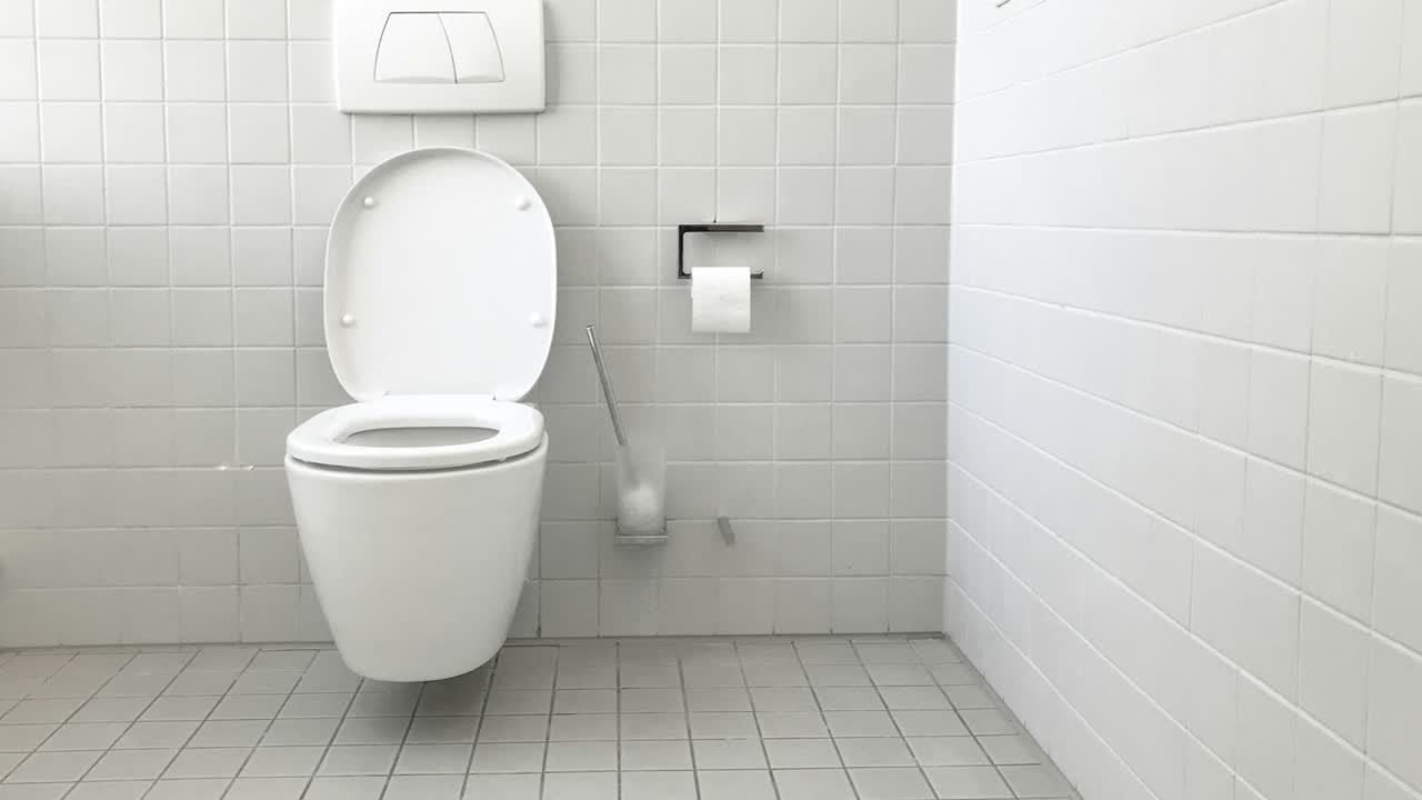 Wand-WC mit Drückerplatte in einem gefliesten Bad